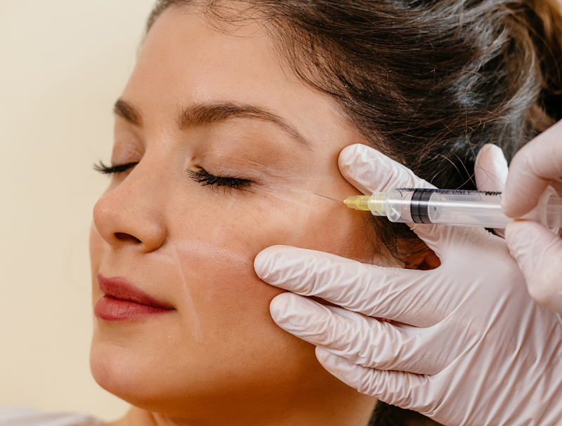 Woman receiving Botox injection near the eye area to reduce crow’s feet, administered by a professional wearing white gloves.